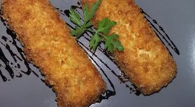 Dos piezas rebozadas y doradas con perejil, sobre plato oscuro con un hilo de reducción