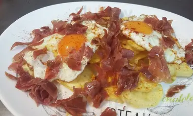 Huevos fritos con jamón sobre patatas, en plato blanco