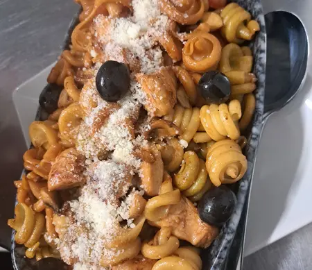 Pasta corta con carne, aceitunas negras y queso rallado, en plato de piedra